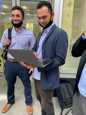 Marc Elliot and Suneel Chakravorty outside of Moira Penza's office building, with a camera crew.