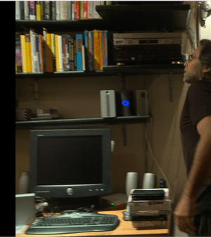 Raniere in his library. The hard drive with the blue light was right above his computer.