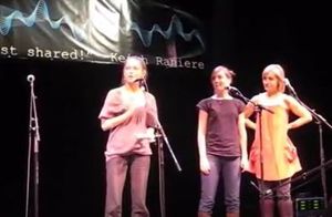 Kristin Kreul, Nicki Clyne, and Allison Mack appear on stage at an a Cappella innovations concert. Note Keith Raniere's name on the banner behind them.