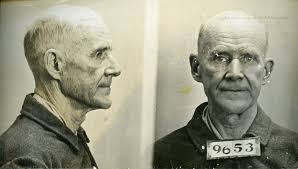 Mugshot of an older man shown in profile and front view, wearing a plain shirt with prisoner number 9653 visible on his chest.