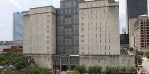 Two beige twin-tower office buildings connected by a darker central core, with trees and a street in the foreground.
