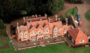 Aerial view of a large, elegant brick mansion surrounded by lush greenery and landscaped gardens.