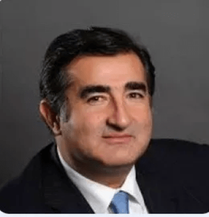 Professional portrait of a middle-aged man with dark hair and a suit, smiling against a neutral background.