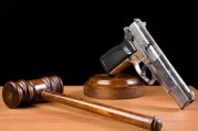 Wooden Gavel And Handgun On Table For Crime Punishment Concept.The background is black.The gun is placed on the right of frame while gavel is seen on the right side.The desk is brown wood.The photo was shot with a full frame DSLR camera in horizontal composition and in studio.Nobody is seen in photo.
